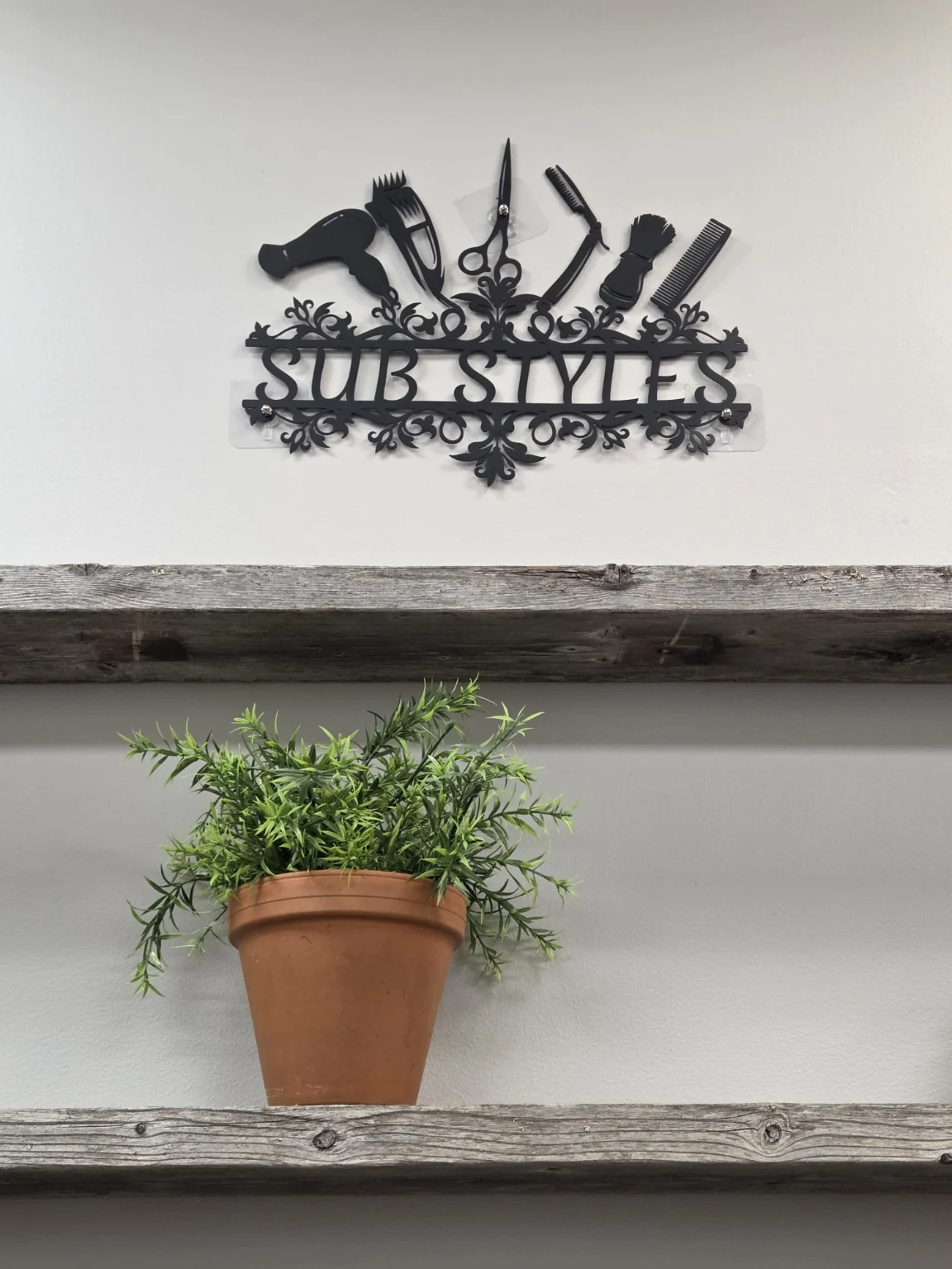 The SUB Styles wall sign above a shelf with a green potted plant.